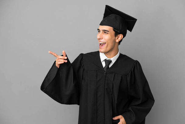 Молодой аргентинский выпускник университета выделяется на сером фоне, указывая пальцем в сторону и представляя продукт - Фото, изображение
