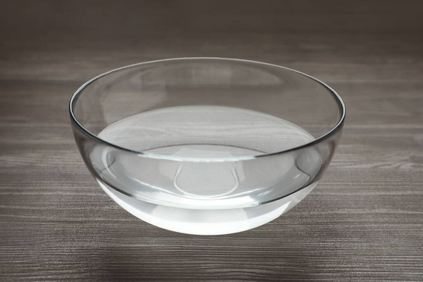 Glass bowl with water on dark wooden table - Foto, afbeelding
