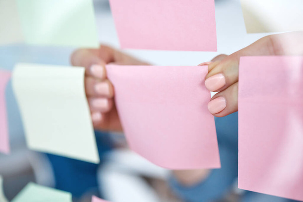 Closeup of unknown business woman using sticky notes on a transparent board to brainstorm in the office. Caucasian professional sticking a note on a visual aid while planning a strategy with ideas. - Foto, imagen