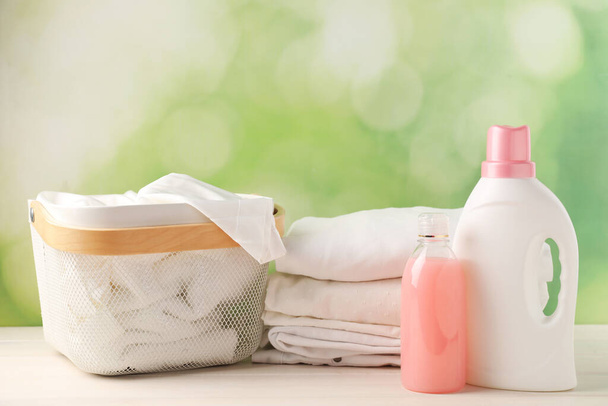 Bottles of laundry detergents and clean clothes on white wooden table - Fotoğraf, Görsel
