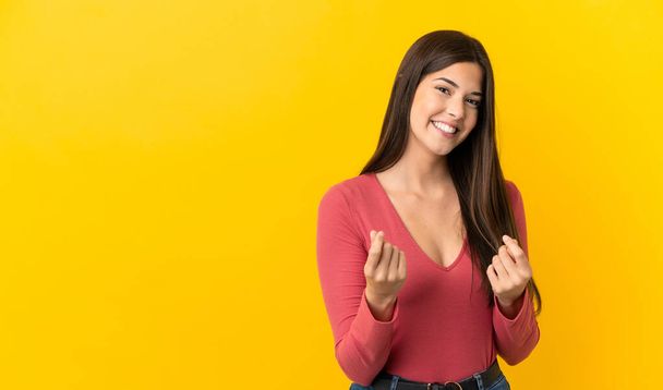 Teenager brasilianisches Mädchen über isoliertem gelben Hintergrund macht Geld-Geste - Foto, Bild