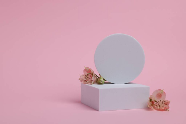 Scene with podium for product presentation. Figures of different geometric shapes and flowers on pink background, space for text - Foto, afbeelding