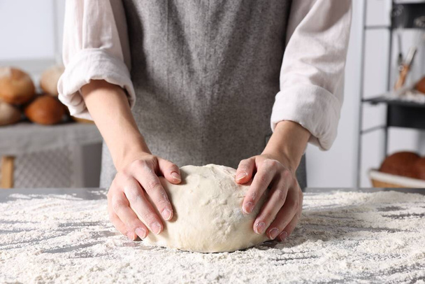 Woman kneading dough at table in kitchen, closeup - Fotó, kép