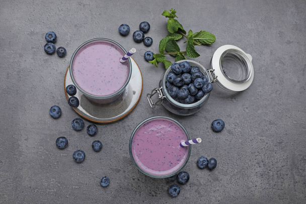 Glasses of blueberry smoothie with mint and fresh berries on grey table, flat lay - Fotó, kép