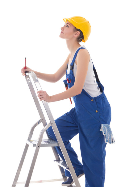 jonge vrouw bouwer in blauwe overall met schroevendraaier op ladder - Foto, afbeelding