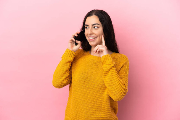 Nuori valkoihoinen nainen käyttää matkapuhelinta eristetty vaaleanpunainen tausta ajattelu idea etsiessään - Valokuva, kuva