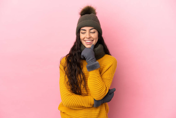 Mladý kavkazský dívka s zimní klobouk izolované na fialovém pozadí dívá do strany a usmívá - Fotografie, Obrázek