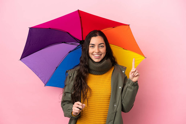 Молода жінка тримає парасольку ізольовано на рожевому тлі, вказуючи на чудову ідею
 - Фото, зображення