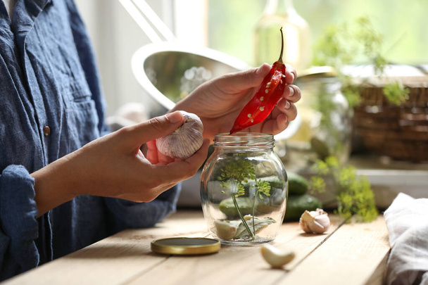 Woman putting pepper into jar in kitchen, closeup - Фото, изображение