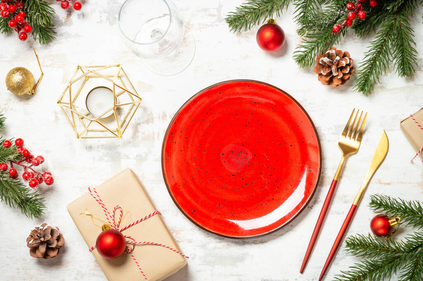 Kerst tafel setting met ambachtelijke plaat, bestek, geschenkdoos en kerstversiering op witte houten tafel. Bovenaanzicht afbeelding. - Foto, afbeelding