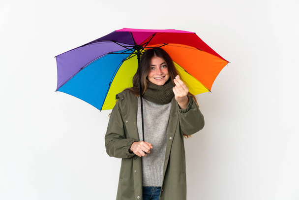 Joven mujer caucásica sosteniendo un paraguas aislado sobre fondo blanco haciendo gesto de dinero - Foto, Imagen