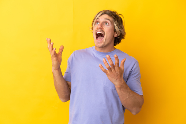 Hombre guapo rubio aislado sobre fondo amarillo con expresión facial sorpresa - Foto, Imagen