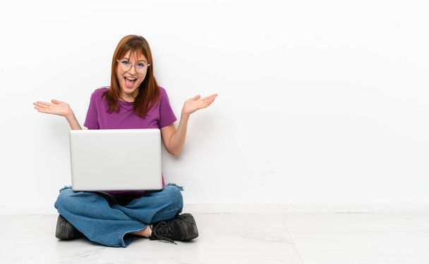 vörös hajú lány laptoppal ül a padlón sokkos arckifejezéssel - Fotó, kép