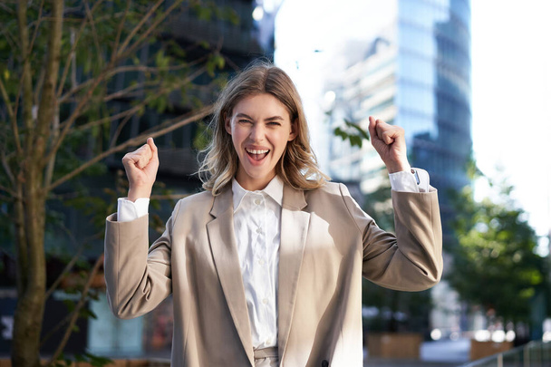 Excited businesswoman screams and celebrates, lifts hands up, does hooray gesture, celebrates victory, achieve goal, stands on street. - Foto, imagen