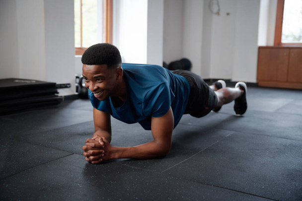 Happy young black man in sportswear doing plank exercises with hands clasped at the gym - Foto, Imagem
