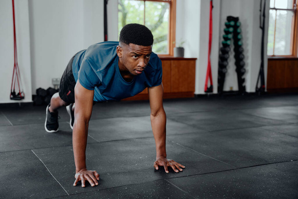 Fit young black man in sportswear doing push-ups at the gym - Фото, зображення