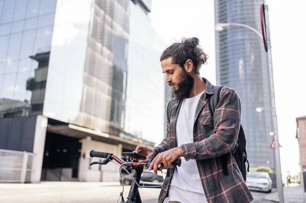 Confident hipster man walking in the street carrying his bike and using his mobile phone. - 写真・画像