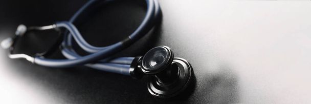 Zwarte medische stethoscoop op een donkere matte achtergrond, close-up. Design element, textuur. Medische hulpmiddelen voor therapeuten - Foto, afbeelding