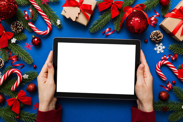 Navidad compras en línea desde casa, manos femeninas sosteniendo la tableta PC con blanco en blanco pantalla vista superior. tableta de mano de mujer con pantalla en blanco, árbol de Navidad y regalos en el fondo. - Foto, imagen