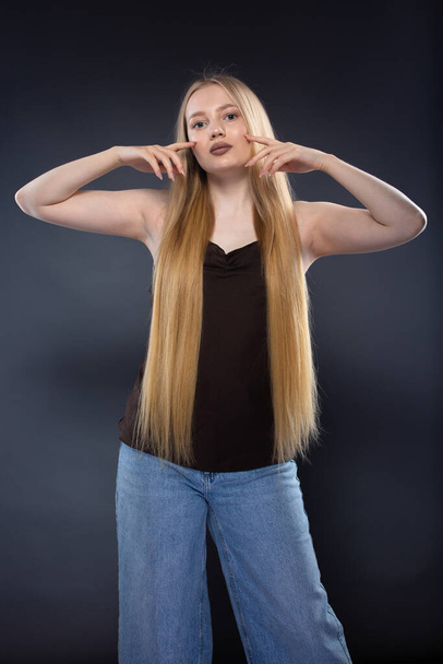 Молодая блондинка в джинсах и коричневом сингле на темно-сером фоне - Фото, изображение