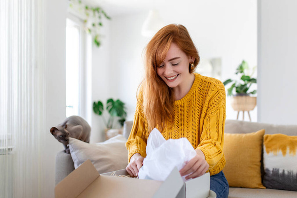 Усміхнена жінка сидить на дивані вдома відкритий поштовий пакет покупки онлайн покупки товарів в Інтернеті, щаслива молода жінка-клієнт розпаковує поштові відправлення, задоволені замовленням або доставкою
 - Фото, зображення