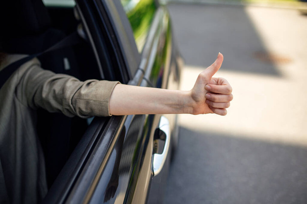 przycięty widok kobiety pokazującej kciuk w górę z okna bocznego podczas prowadzenia samochodu na niewyraźnym pierwszym planie - Zdjęcie, obraz
