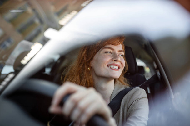 Όμορφη νεαρή γυναίκα οδηγεί το νέο της αυτοκίνητο το ηλιοβασίλεμα. Γυναίκα στο αυτοκίνητο. Κοντινό πλάνο πορτρέτο της ευχάριστης γυναίκας με ευχάριστη θετική έκφραση, γυναίκα σε casual φορούν οδήγηση αυτοκινήτου - Φωτογραφία, εικόνα