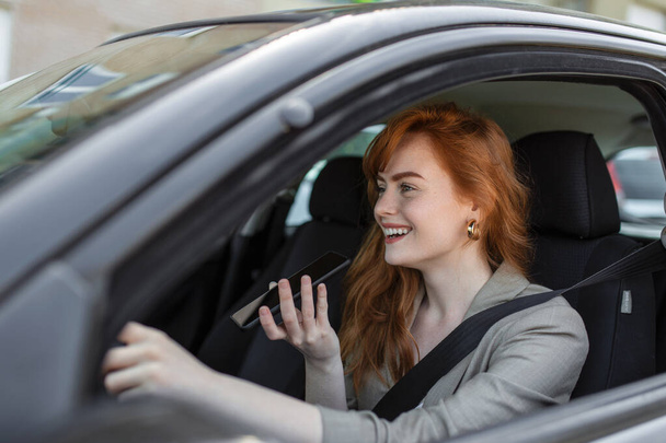 Primer plano de la mujer usando el teléfono móvil y hablando en el altavoz mientras conduce el coche. Mujer hablando en altavoz en el coche mientras conduce - Foto, Imagen