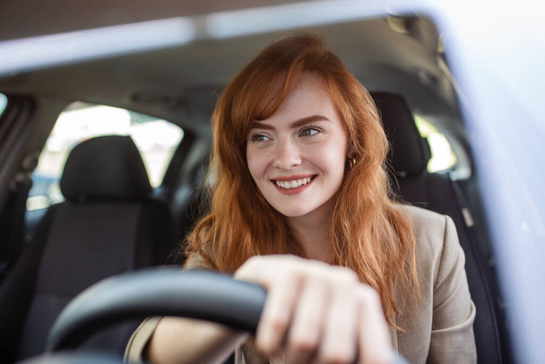 Beautiful young woman driving her new car at sunset. Woman in car. Close up portrait of pleasant looking female with glad positive expression, woman in casual wear driving a car - Photo, Image