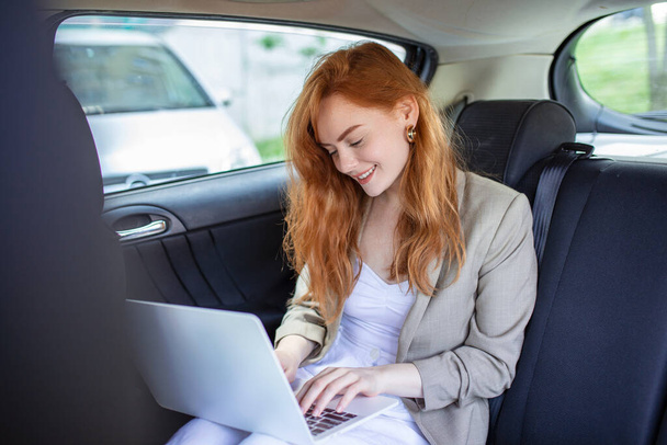 Töprengő üzletasszony laptoppal a hátsó ülésen. Egy fiatal nő laptopot használ egy autóban.. - Fotó, kép