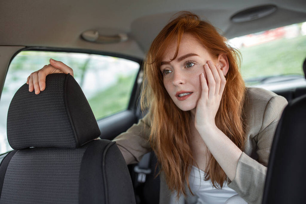 mujer asustada sosteniendo la mano en la cabeza mientras monta en coche en primer plano borroso - Foto, Imagen