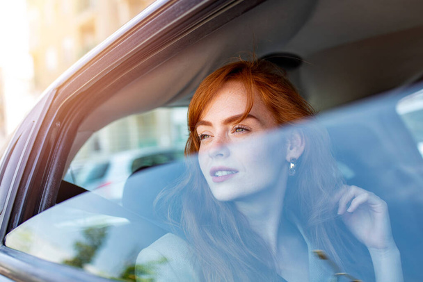 Bela jovem empresária sentada no banco de trás de um carro e olhando para fora da janela. Executiva mulher viajando de táxi. - Foto, Imagem