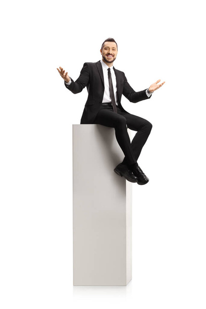 Cheerful businessman sitting on a tall white column and smiling at camera isolated on white background - Foto, afbeelding