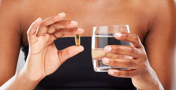 Zorg voor uw gezondheid een supplement per keer. een onherkenbare persoon die een tablet tegen een grijze achtergrond inneemt - Foto, afbeelding