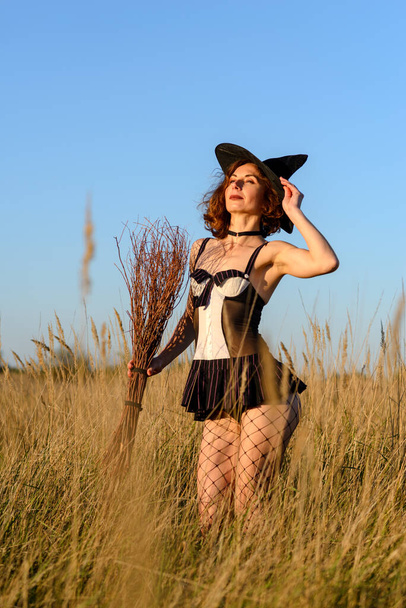 Sexy young woman in a witch's hat and a broom in the field. Concept for halloween. - Foto, afbeelding