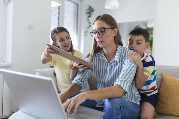 Stresszes nő gyerekekkel dolgozik otthonról.Fáradt fiatal anya ül a kanapén, és dolgozik a laptop és dokumentumok, míg a kisgyerekek szórakozás és zajongás - Fotó, kép
