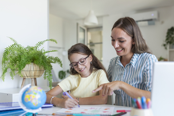 Cute girl with mother doing homework at home. A mother helps her little daughter to do her homework for the school. Education and family concept - Фото, зображення