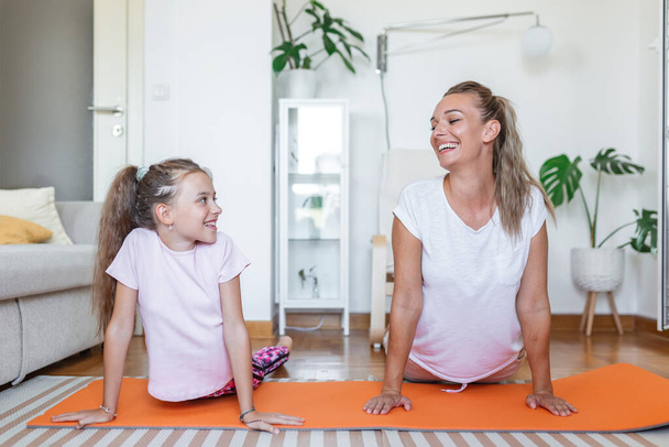 Veselý fit žena a malá dcera dělá výpady cvičení při tréninku společně před notebookem v moderním bytě. rodinná matka a dcera jsou zapojeny do fitness - Fotografie, Obrázek