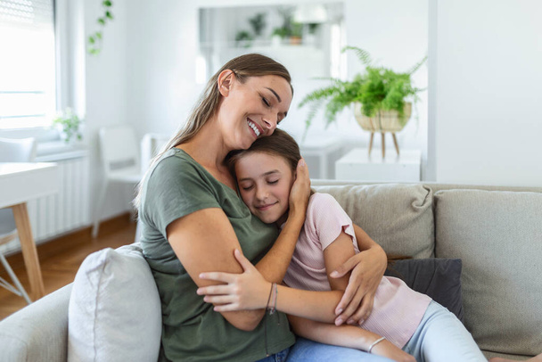 I love you so much. Portrait of happy young mother piggybacking cute smiling little daughter in living room, affectionate school age girl embracing beloved millennial female nanny or foster mom - Фото, изображение