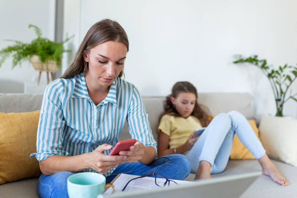 junge Mutter arbeitet zu Hause mit ihrem Kind auf dem Sofa, während sie eine E-Mail schreibt. Junge Frau arbeitet von zu Hause aus, während sie während der Covid-19-Gesundheitskrise unter Quarantäne steht - Foto, Bild