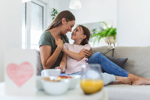 I love you so much. Portrait of happy young mother piggybacking cute smiling little daughter in living room, affectionate school age girl embracing beloved millennial female nanny or foster mom - Photo, Image