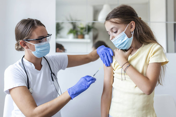 医者の予防接種の女の子。COVID-19ワクチンを患者の腕に注射する。女の子で医療マスク取得ワクチン接種に対してcovid-19,医師注射のコロナウイルスワクチンで病院. - 写真・画像