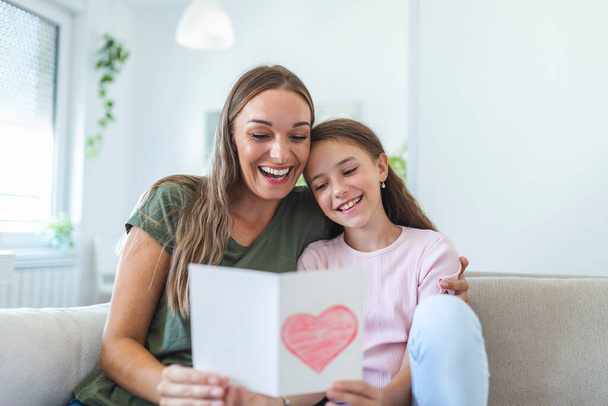 Happy mother's day! Child daughter congratulates mom and gives her postcard. Mum and girl smiling and hugging. Family holiday and togetherness. - Photo, Image