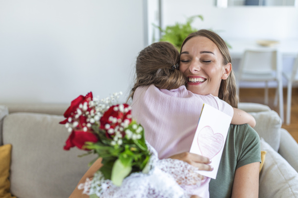 I love my you mom! Attractive young woman with little cute girl are spending time together at home, thanking for handmade card with love symbol and flowers. Happy family concept. Mother's day. - Photo, Image