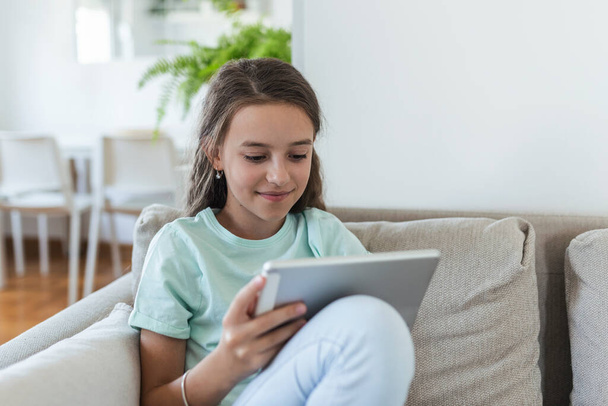 cute little happy girl smile sitting down on sofa using looking digital tablet pad in the living room at home. family activity concept. - Foto, imagen