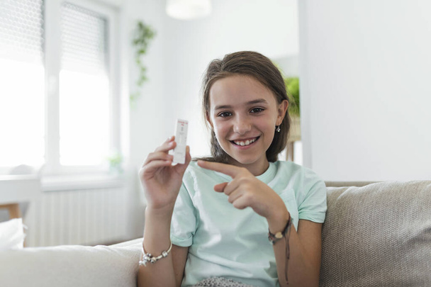 Un primo piano di una ragazzina con un dispositivo negativo al test. Giovane ragazza felice mostrando il suo negativo Coronavirus Covid-19 test rapido. Coronavirus - Foto, immagini