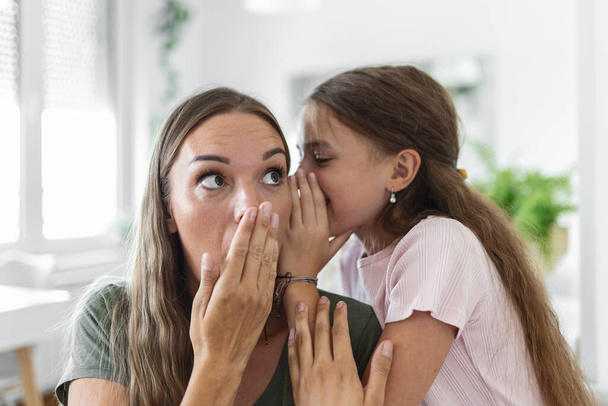 Close up image amazed mother hears incredible news from little daughter, kid girl share secret telling something interesting while mom open mouth feels surprised, trust, confidant person, fun concept - Photo, Image