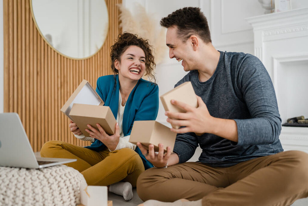 young couple man and woman boyfriend and girlfriend or husband and wife exchange gifts at home giving presents to each other and opening box happy smile celebrate valentine holiday or birthday - Fotó, kép