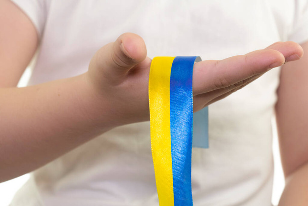 A girl in a white T-shirt holds a yellow-blue textile ribbon in her hands. State flag of Ukraine. National symbol of Ukraine. Patriot. Close-up - Fotografie, Obrázek