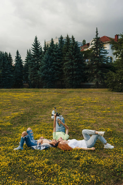 Influencerzy nagrywania wideo z aplikacji telefonicznej podczas leżenia w parku na zielonym trawniku. Koncepcja mediów społecznościowych. Blogi, wideoblogi. Szczęśliwe twarze, pozytywne - Zdjęcie, obraz